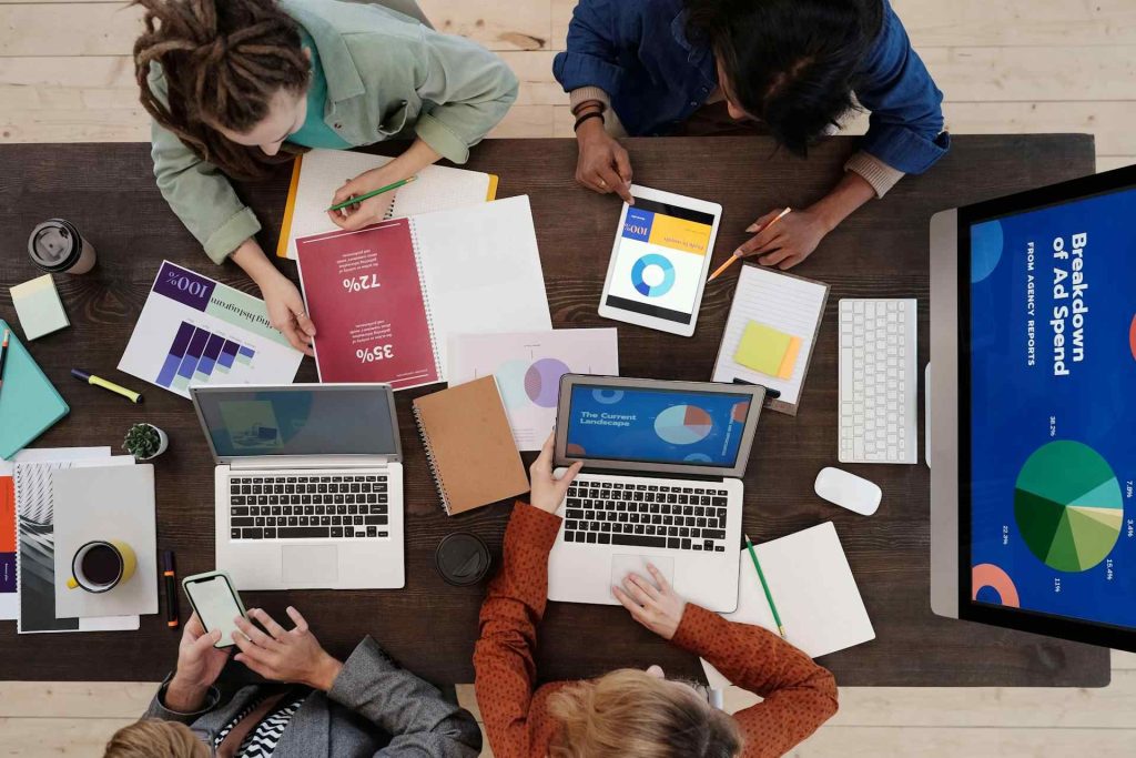 A Top-View Of a Team Collaborating At a Table With Laptops, Tablets, And Documents abot Digital Advertisements - Boost Online Visibility