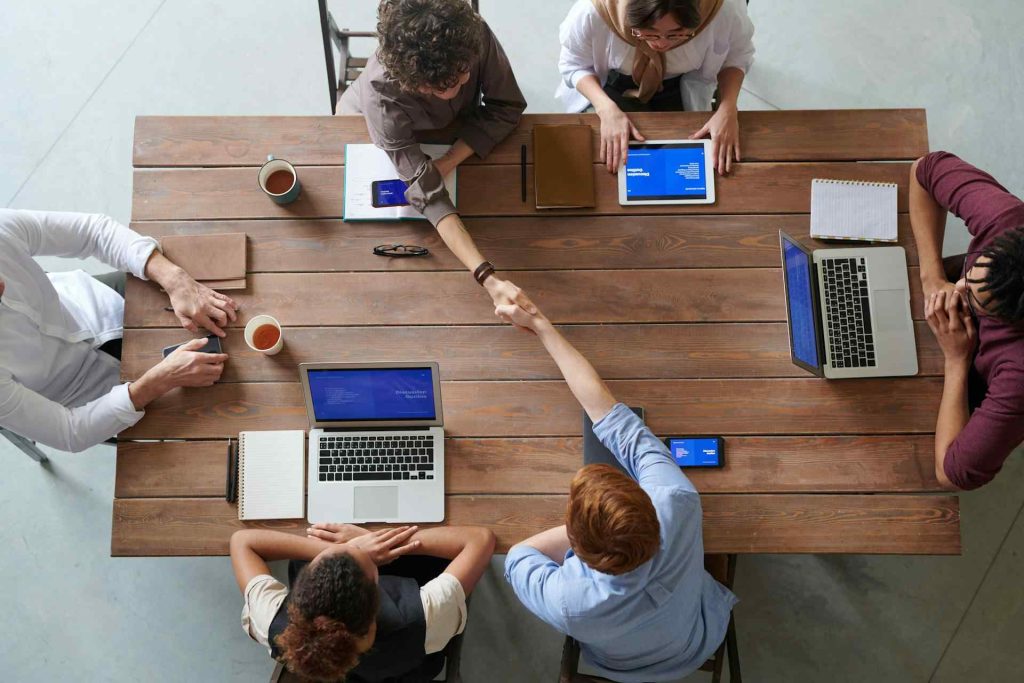 27 DiGi IT Consultation 1 Top-down View Of a Team Meeting With Laptops And Handshakes At a Wooden Table