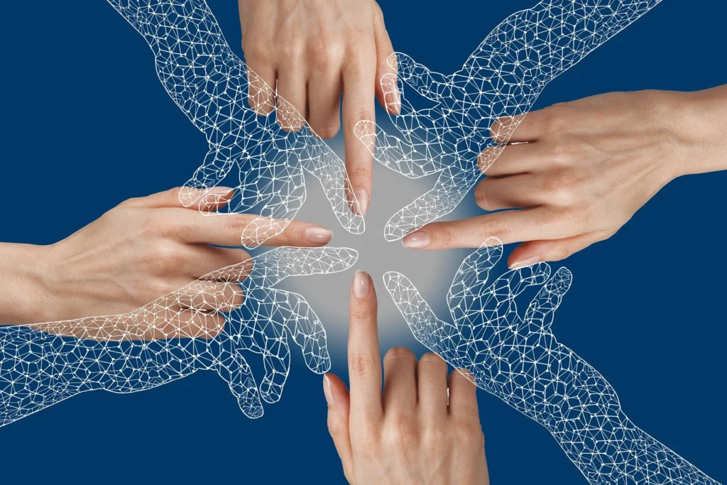 Multiple hands, real and wireframe, reach towards a glowing center on a blue background, symbolizing connection and collaboration.