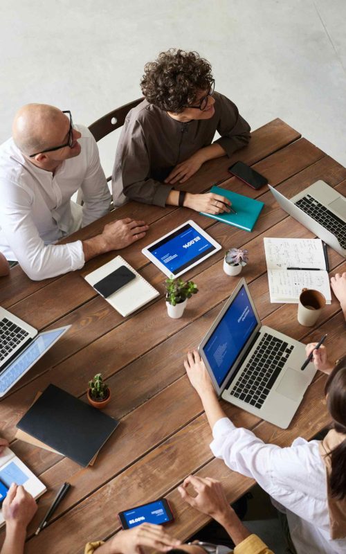 Persons 1 A Top-Down View Of a Business Meeting With Laptops, Tablets, And Notes On a Wooden Table